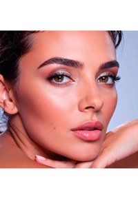 Gros plan sur un visage avec une peau brune chaude, des sourcils bien dessinés, un maquillage des yeux audacieux et des lèvres roses brillantes. Une texture lisse et un éclairage doux mettent en valeur les traits.