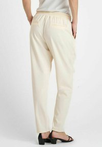 Beige, elastische taille, taps toelopende broek met twee achterzakken. Gladde stof, minimalistisch ontwerp, enkel lengte, met een omslag aan de onderkant.