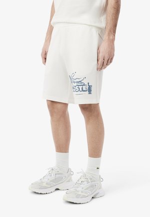 Pantalones cortos de algodón blancos con el logo azul de Lacoste, con un ajuste relajado y cintura elástica. Combinados con zapatillas blancas y calcetines.