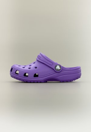 Violetinė lengva medinė kurpa su ventiliacijos angomis ir reguliuojama kulno juostele ant neutralaus fono.