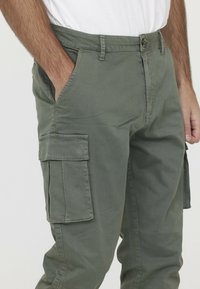 Cargo-broek in olijfgroen katoen met een gladde textuur. Voorzien van zijzakken en een knoopsluiting. Gemakkelijk gesneden met riemlussen.