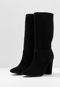Černé semišové kotníkové boty s hladkým povrchem, špičatou špičkou a blokovým podpatkem. Mají vysokou holení a minimalistický design.