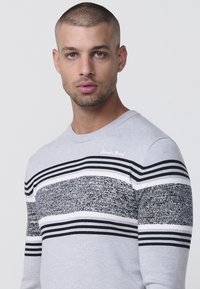 Suéter gris con cuello redondo, patrones a rayas en blanco y negro, sección media texturizada y un diseño ajustado.