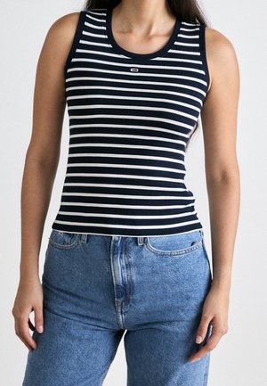 Granatowo-biały tank top w paski o prążkowanej fakturze, z okrągłym dekoltem i logo na piersi, zestawiony z jasnoniebieskimi dżinsami.