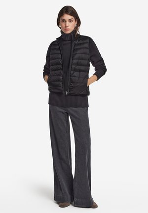Svart pufferväst med horisontell kviltad design, dragkedja, bärs över en svart polo. I kombination med vida mörkgrå jeans och ankelstövlar.