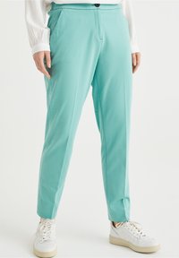 Ljus tealbyxor i ett mjukt material, med en avslappnad passform, framfickor och knäppning. Matchad med vita sneakers.