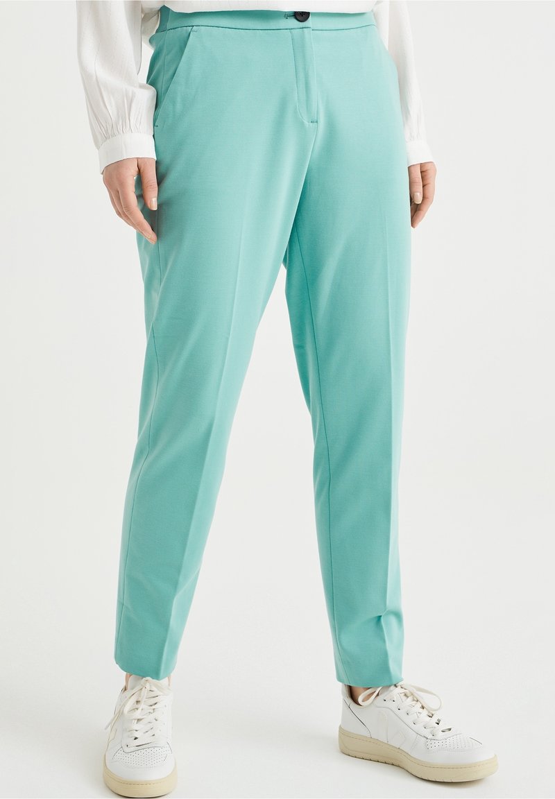 Ljus tealbyxor i ett mjukt material, med en avslappnad passform, framfickor och knäppning. Matchad med vita sneakers.