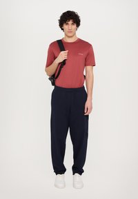 Röd bomulls T-shirt med rund halsringning, kombinerad med marinblå joggingsbyxor med elastiskt midjeband och sidofickor. Vita sneakers fullbordar outfiten.