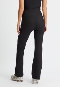 Pantalones de yoga negros acampanados con textura de canalé y una cinturilla alta, combinados con zapatillas deportivas plateadas. Diseño simple sin patrones.