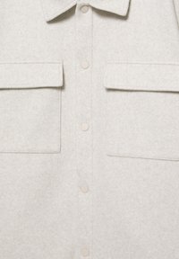 Jasna beżowa wełniana kurtka z kołnierzem, przednimi zatrzaskami oraz dwoma dużymi kieszeniami z klapami na piersi.