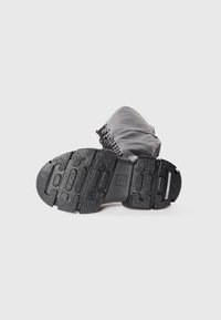 Black leather boot featuring a textured rubber sole with tread patterns and a lacing detail at the top.