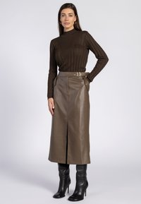 Bruine geribbelde coltrui gecombineerd met een bruin leren midi-rok met een voorkeursplit en een ceintuur in de taille. Zwarte haklaarzen maken de outfit compleet.