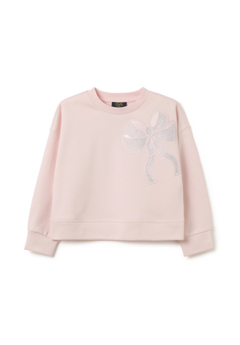 Sudadera corta de color rosa claro en tejido suave con cuello redondo, que presenta un diseño de lazo blanco con embellishments en el lado izquierdo.