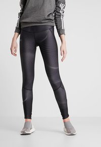 Leggings neri con un motivo a pois dinamico, caratterizzati da un'alta vita e un design aderente. Abbinati a una felpa grigia e scarpe sportive.