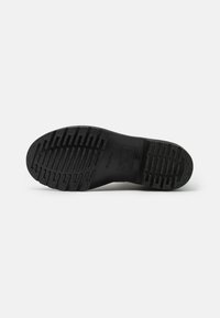 Suela de zapato de goma negra con patrones de surcos profundos tanto horizontales como verticales, que presenta detalles de marca en relieve en el centro.