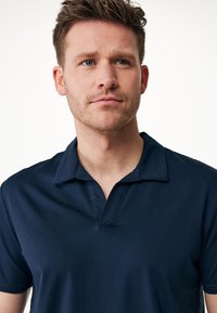 Marinblå polo skjorta tillverkad av ett glatt tyg, med en kort, öppen krage och en subtil sömdetalj vid halsringningen.