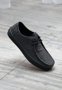 Μαύρο sneaker με υφή κροκόδειλου, με στρογγυλεμένη μύτη, δέσιμο με κορδόνια και λαστιχένια σόλα.