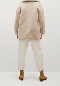 Beige faux fur frakke med afslappet pasform, båret over kridhvide, opkrøllede bukser og tan ruskinds ankelstøvler med blokhæl.