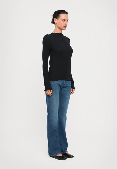 Black long-sleeve top with scalloped edges, paired with flared blue jeans. The fabric appears soft with a fitted silhouette. Black flats complete the look.