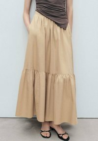 Gonna midi beige a strati realizzata in tessuto leggero. Presenta una vita elasticizzata e tasche laterali. Abbinata a sandali neri.