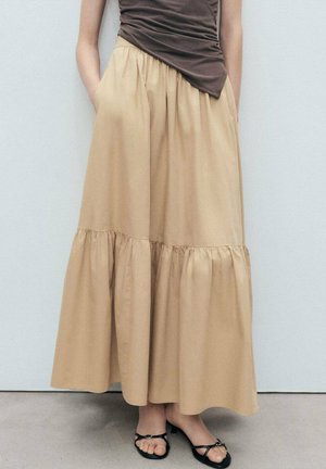 Gonna midi beige a strati realizzata in tessuto leggero. Presenta una vita elasticizzata e tasche laterali. Abbinata a sandali neri.