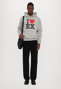 Felpa grigia con cappuccio e grafica nera e rossa "I ♥ my EX", abbinata a pantaloni neri e scarpe nere, e una borsa a spalla.