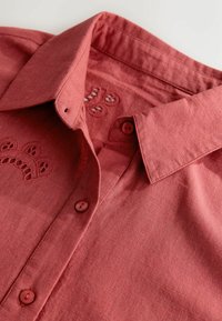 Puuvillane särk summutatud korallitoonis, millel on terav krae, kaks nuppu ja kaeluse ümbruses tikitud lillemustrid.