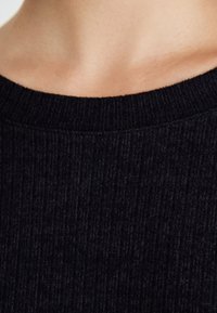 Black ribbed knit sweater with a wide, textured neckline. The fabric displays vertical lines, emphasizing its soft texture and structured design.