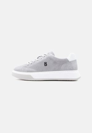 Zapatilla deportiva de ante gris claro con laterales perforados, suela acolchada blanca, cierre de cordones y logotipo con la letra "B" en negro en el lateral.