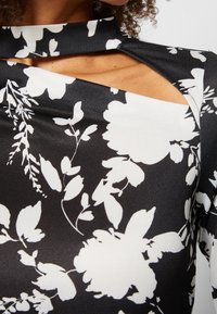 Zwart-witte bloes met bloemenpatroon, gemaakt van een gladde stof, met een hoge kraag en asymmetrische snit met gedeeltelijke schouderbekleding.