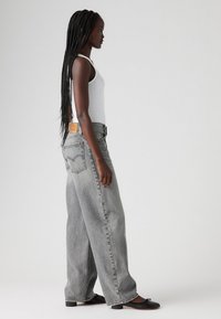 Gray denim wide-leg jeans with a high waist, prominent stitching, and a leather patch on the back. Paired with a white tank top and black shoes.