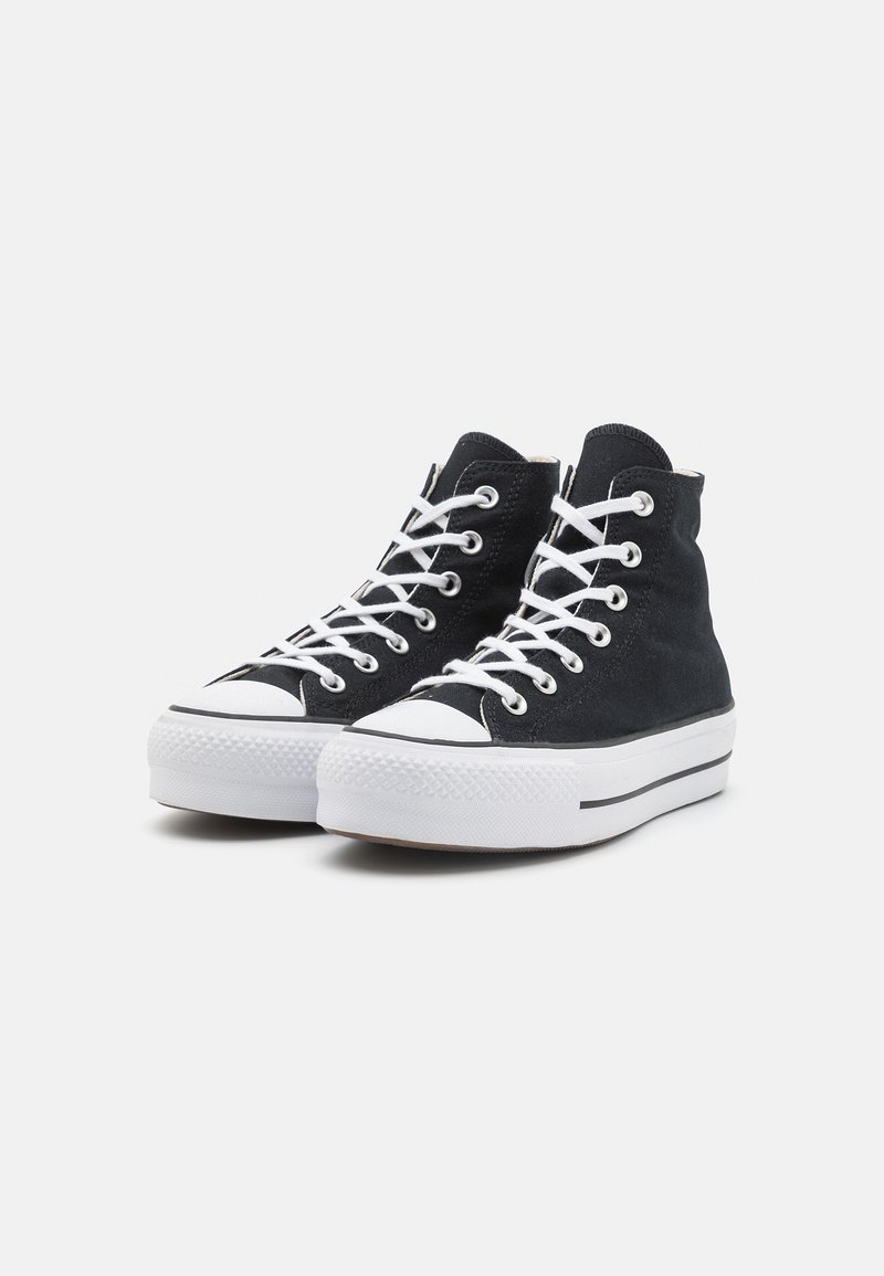 Baskets montantes noires avec des lacets blancs, bouts en caoutchouc, tissu noir texturé et une semelle épaisse blanche avec une bande noire.