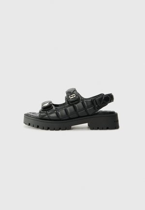 Sandalias negras con un diseño acolchado, correas ajustables y suelas de goma gruesas. Presentan acentos metálicos y un acabado elegante.