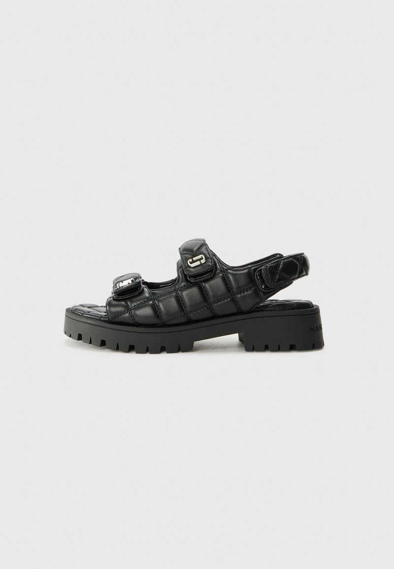 Sandalias negras con un diseño acolchado, correas ajustables y suelas de goma gruesas. Presentan acentos metálicos y un acabado elegante.