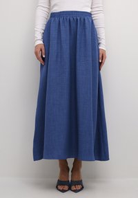 Blå, lang maxi nederdel lavet af tekstureret stof med elastisk talje, parret med åbne blå hæle.