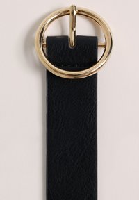 Črn usnjen pas z velikim okroglim zlatim sponko, ki ima teksturirano površino in gladko ter elegantno zasnovo.