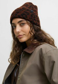 Brązowa i czarna czapka beanie w leopardzi wzór, miękka w dotyku, dopasowany krój, zestawiona z brązową kurtką z kołnierzem z korduroyu.