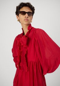 Piros fodros ruha hosszú ujjakkal és magas gallérral. Könnyű anyagból készült, térd hosszúságú, gathered derékkal és finom textúrával.