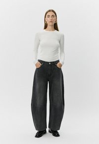 Črne široke denimske hlače z visokim pasom, dvema stranskima žepoma in gumbom, v kombinaciji z oprijetim belim dolgim rokavom.