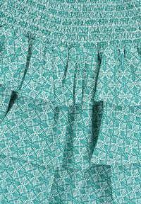 Een gerimpelde jurk van lichtteal stof met een bladerenpatroon in het wit, en geplooide details bij de buste voor textuur en beweging.