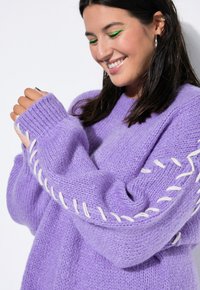 Maglione viola lavorato a maglia con cuciture bianche lungo le maniche, con polsini a coste e una finitura testurizzata. Design morbido e oversize.