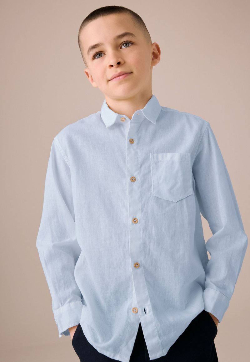 Lyseblå skjorte med knapper lavet af blødt stof, med brystlomme, lange ærmer og rundet kant, samt brune knapper.