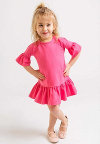 Jasnoróżowa sukienka z krótkim rękawem, z falbaną i bufkami, wykonana z miękkiego materiału. Połączona z jasnoróżowymi baletkami.