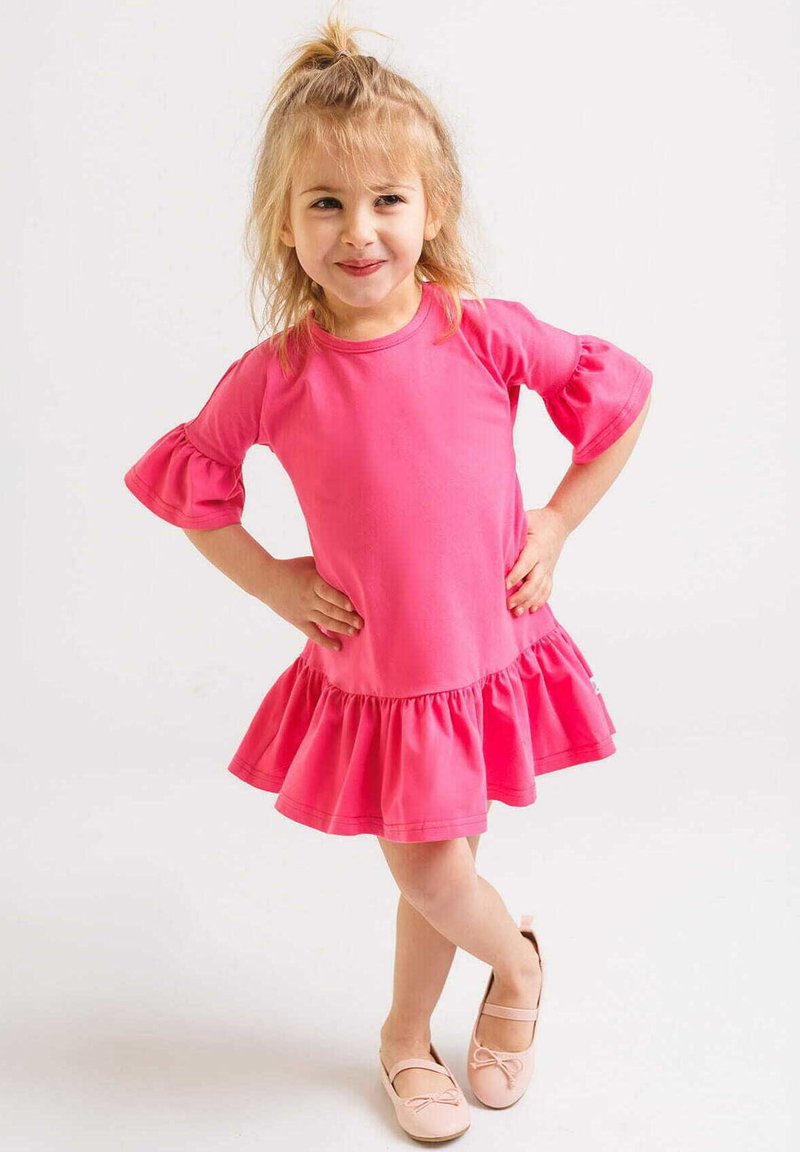 Jasnoróżowa sukienka z krótkim rękawem, z falbaną i bufkami, wykonana z miękkiego materiału. Połączona z jasnoróżowymi baletkami.