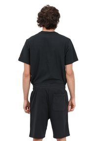 Tricou din bumbac negru cu mâneci scurte și guler rotund, asociat cu șorturi negre cu talie elastică și un buzunar la spate.