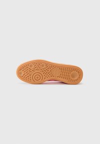Sportsko med sål i orange gummi, der har et tekstureret mønster og cirkulære detaljer. Kanten buer let opad. Designet til optimal traction.