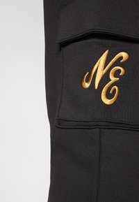 Schwarzer Sweatshirt mit einem großen, goldenen, gestickten "NE" auf der Brusttasche, aus texturiertem Stoff und flachen Nähten.