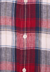 Rood en marineblauw geruite overhemden met witte, blauwe en groene accenten. Heeft een klassieke kraag en witte knopen. Gemaakt van katoen.