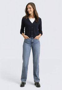 Moteriškas tamsiai mėlynas ribotas kardiganas su sagų užsegimu, derinamas su šviesiai mėlynomis tiesiomis džinsomis ir juoda avalyne. Paprastas dizainas, laisvas stilius.