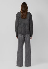 Grijze gebreide trui met geribde manchetten en zoom, gecombineerd met grijze, wijde jeans. Glad textuur, relaxte pasvorm en minimalistisch ontwerp.